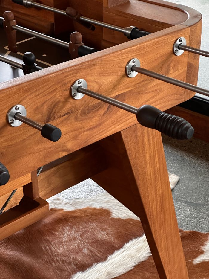 Detailed view of wooden foosball table with metal rods and handles indoors.
